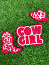 Set of three cow-girl themed iron-on patches: a detailed pink and white cowboy hat, a pink cowboy boot, and a patch with the words COWGIRL in bold pink letters on a white background.