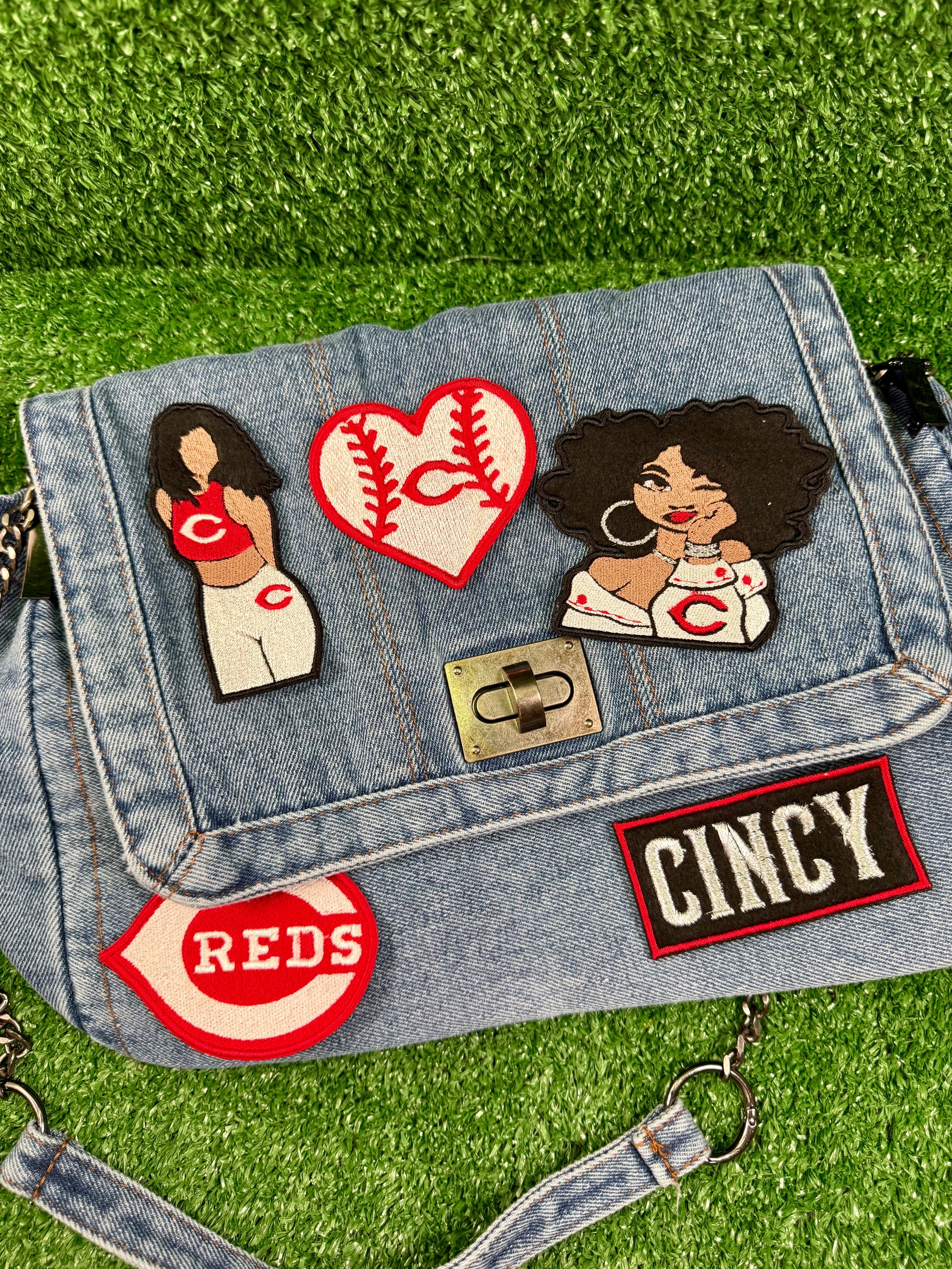 Denim bag with patches including 'Reds' and 'Cincy' on a grass background