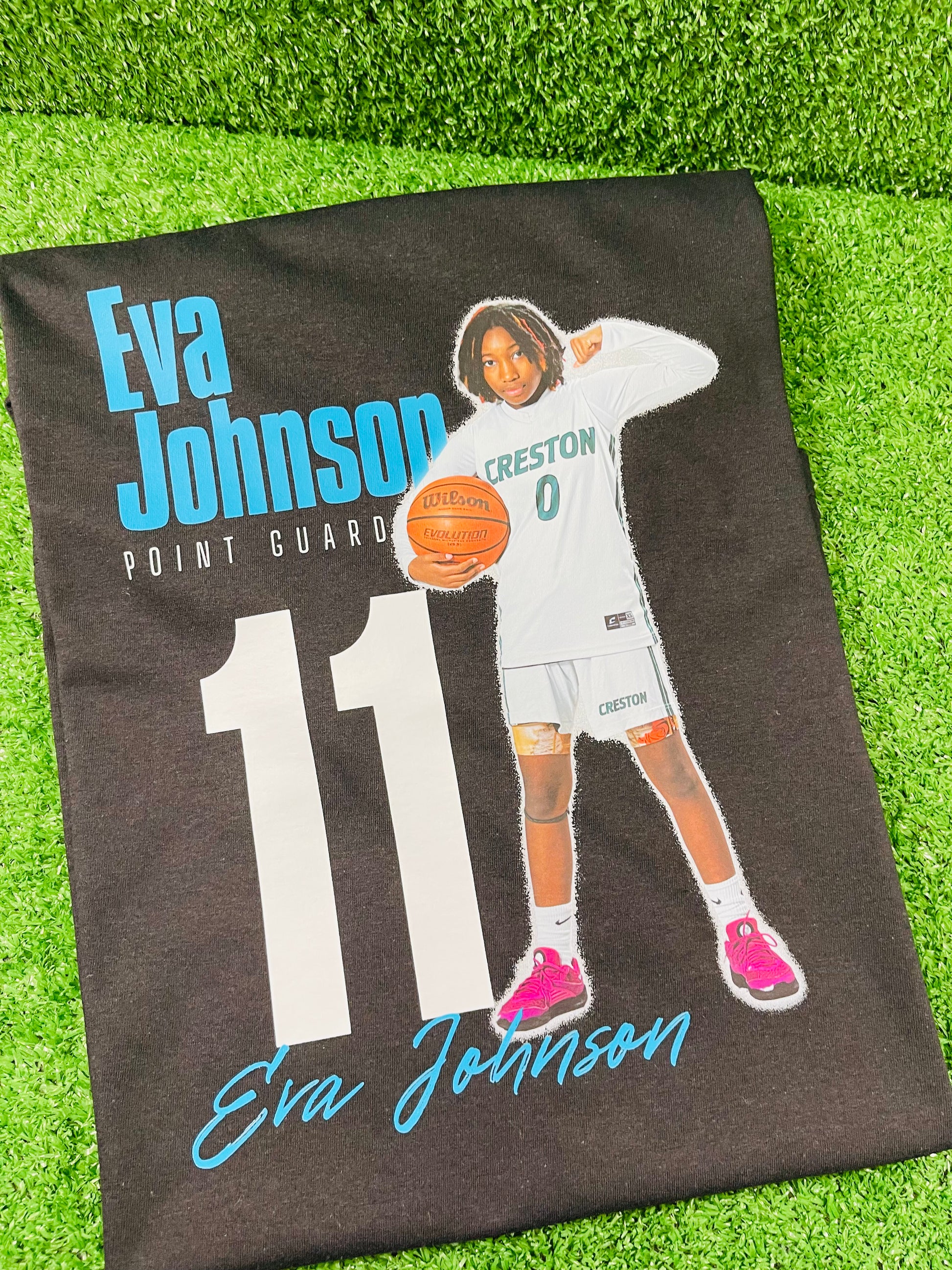 Custom black basketball shirt featuring a young female atahlete in uniform holding a basketball with her name Eva Johnson position, and jersey humber printed in bold graphic text. 