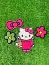 A set of four embroidered patches displayed on bright green grass. The set includes a white kitty wearing a pink hoodie, and holding an iced coffee, a pink bow, a green flower with a yellow center, and a pink flower with a yellow center. The patches are digitized and embroidered with high-quality stitching.