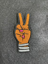 Custom embroidered Deuces patch depicting a hand with two fingers raised in a peace sign adorned with bangles and matching nails.