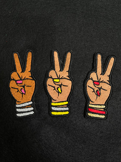 Custom embroidered Deuces patches depicting a hand with two fingers raised in a peace sign adorned with bangles and matching nails.