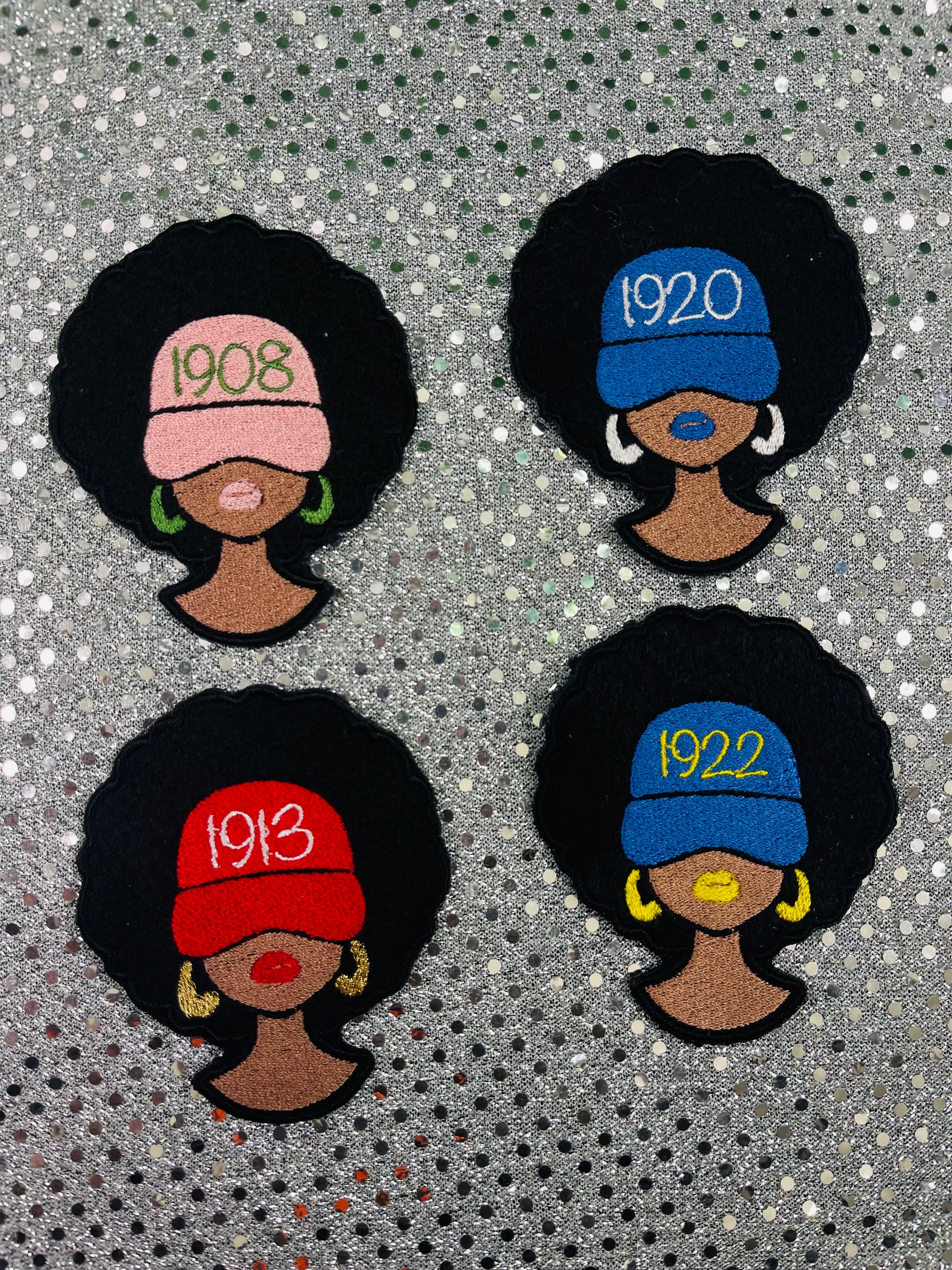 Four embroidered patches of women with styled hair and vintage hats on a textured background. The women are wearing different caps with the year their sorority was founded. 