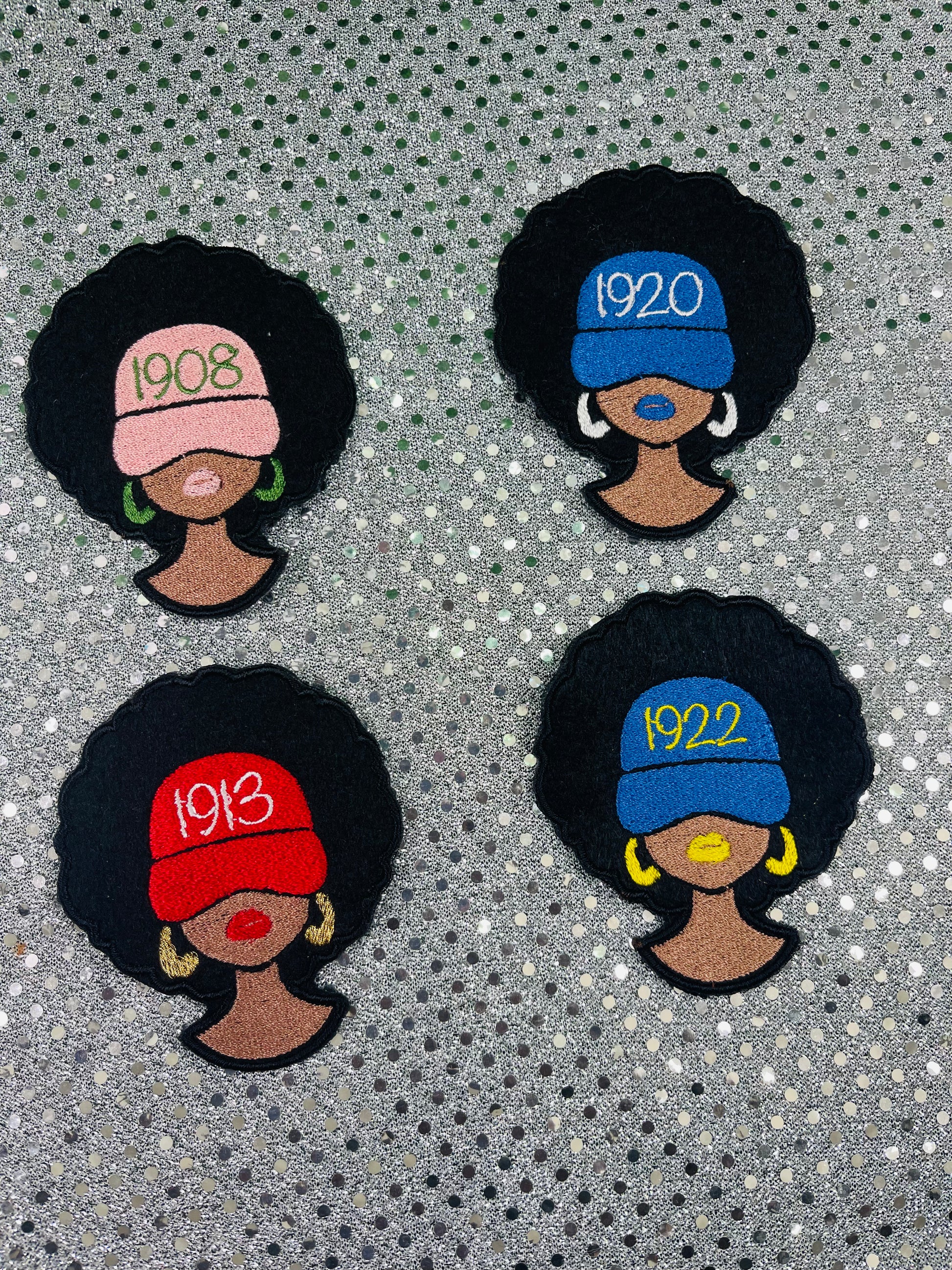 Four embroidered patches of women with different colored hats and years on a textured background. NPHC Sorority Patches. 