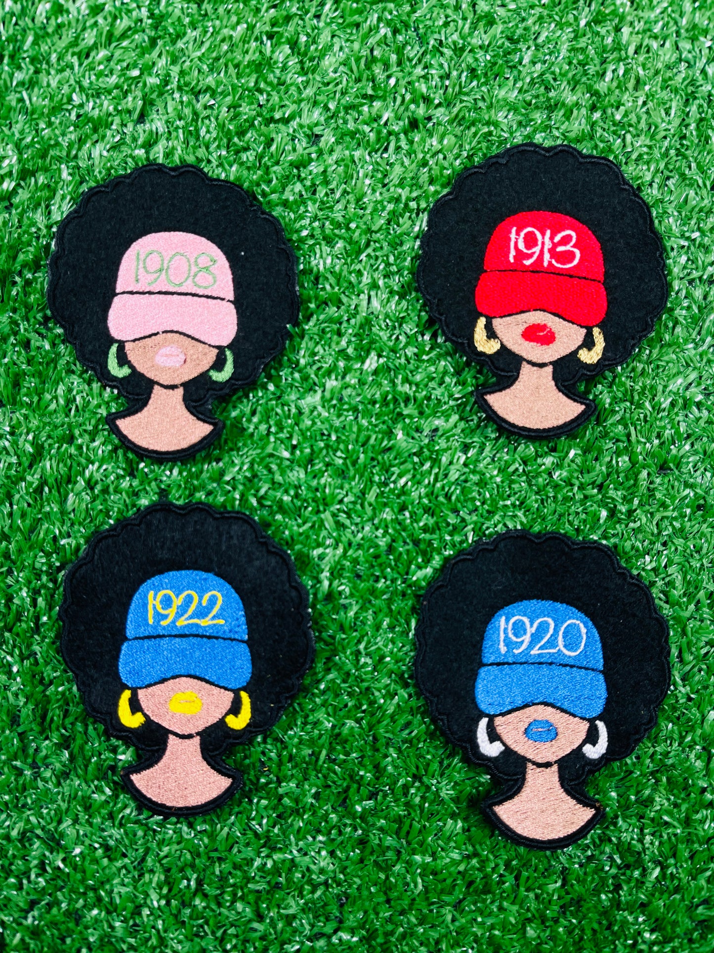 Four decorative pins with black hair, colorful hats, and numbers on a green grass-like background.