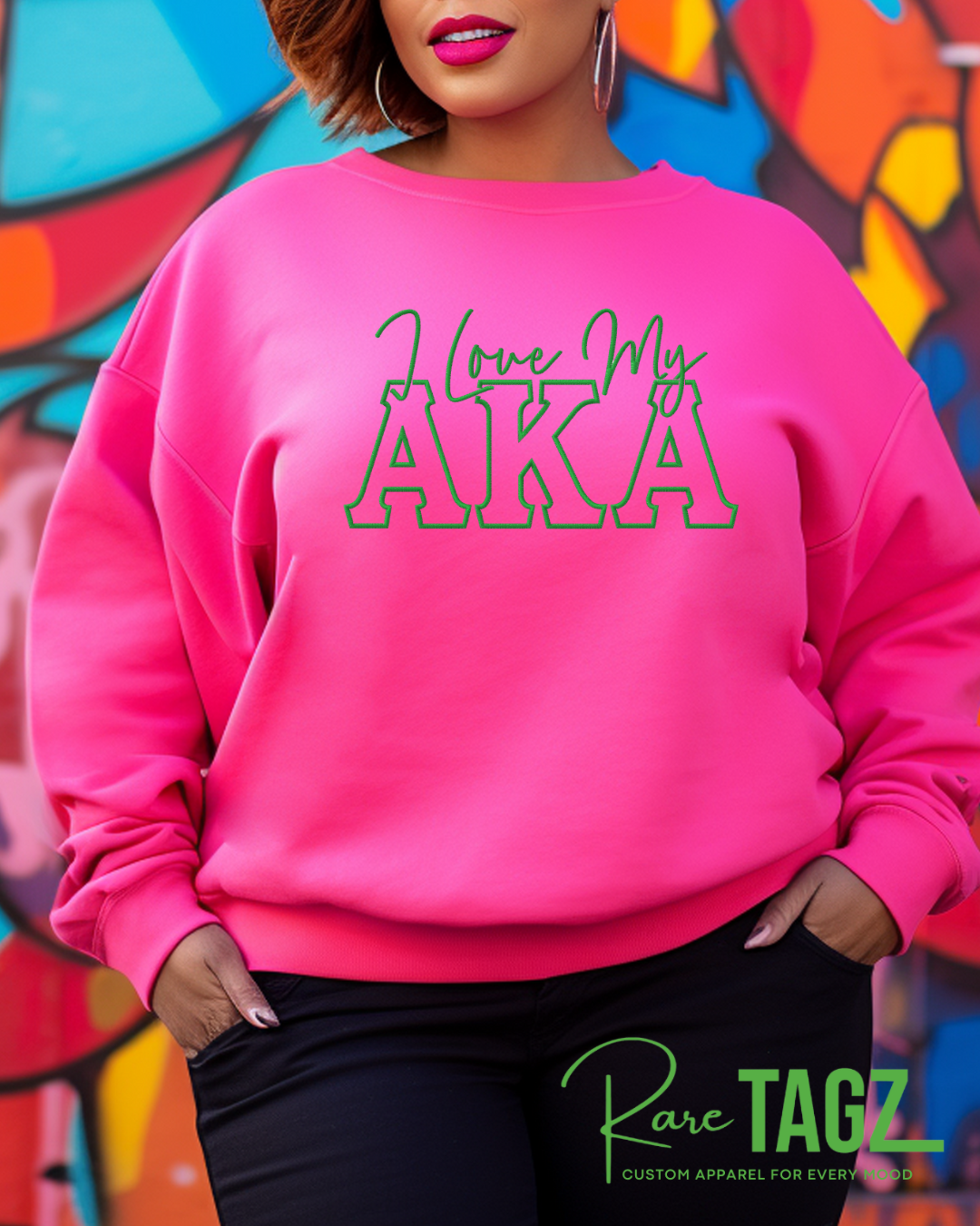 Person wearing a pink sweatshirt with 'I love my AKA' text in front of a colorful mural.
