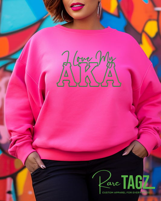 Person wearing a pink sweatshirt with 'I love my AKA' text in front of a colorful mural.