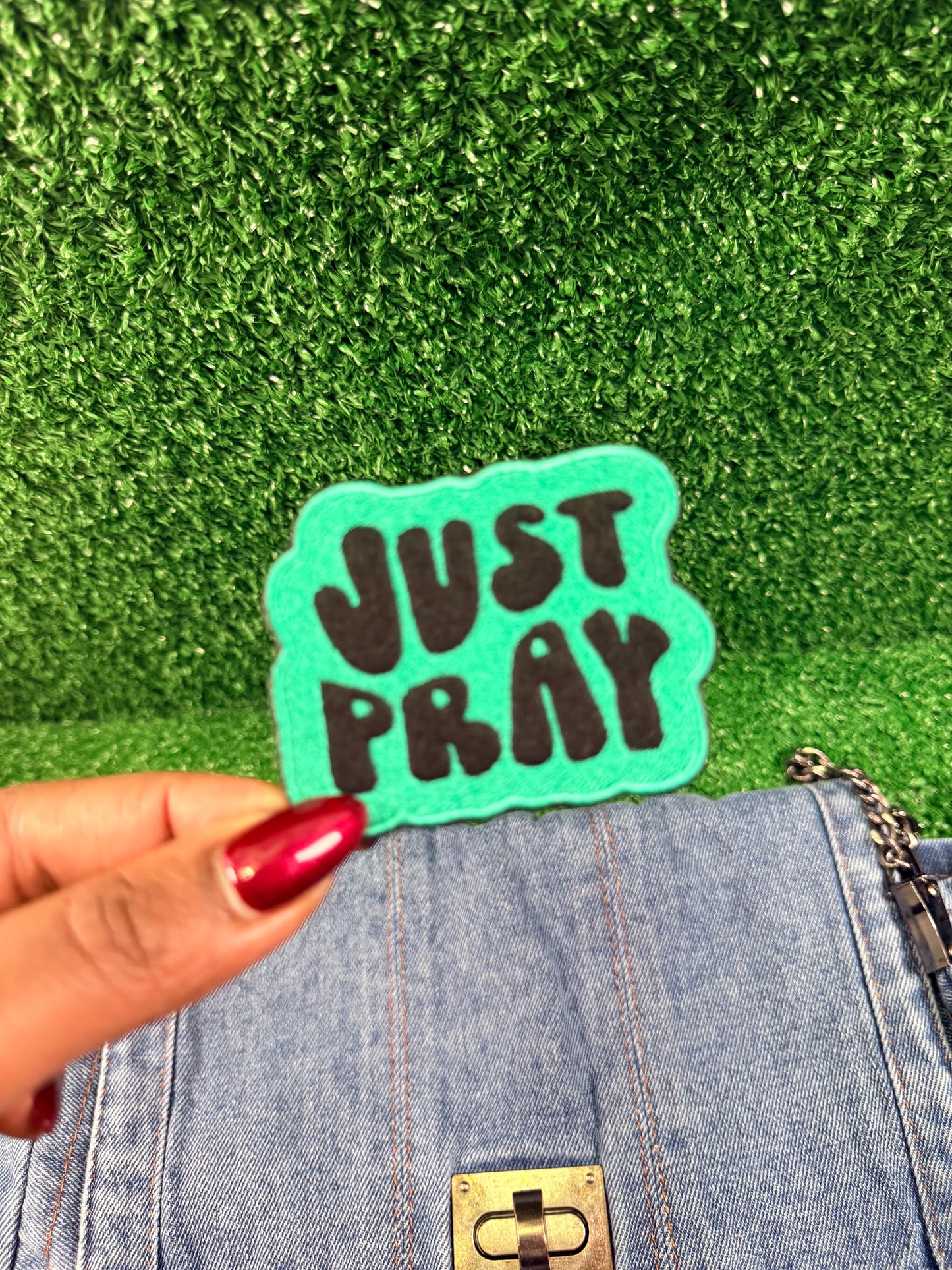 Teal patch with 'JUST PRAY' text held over a green textured background