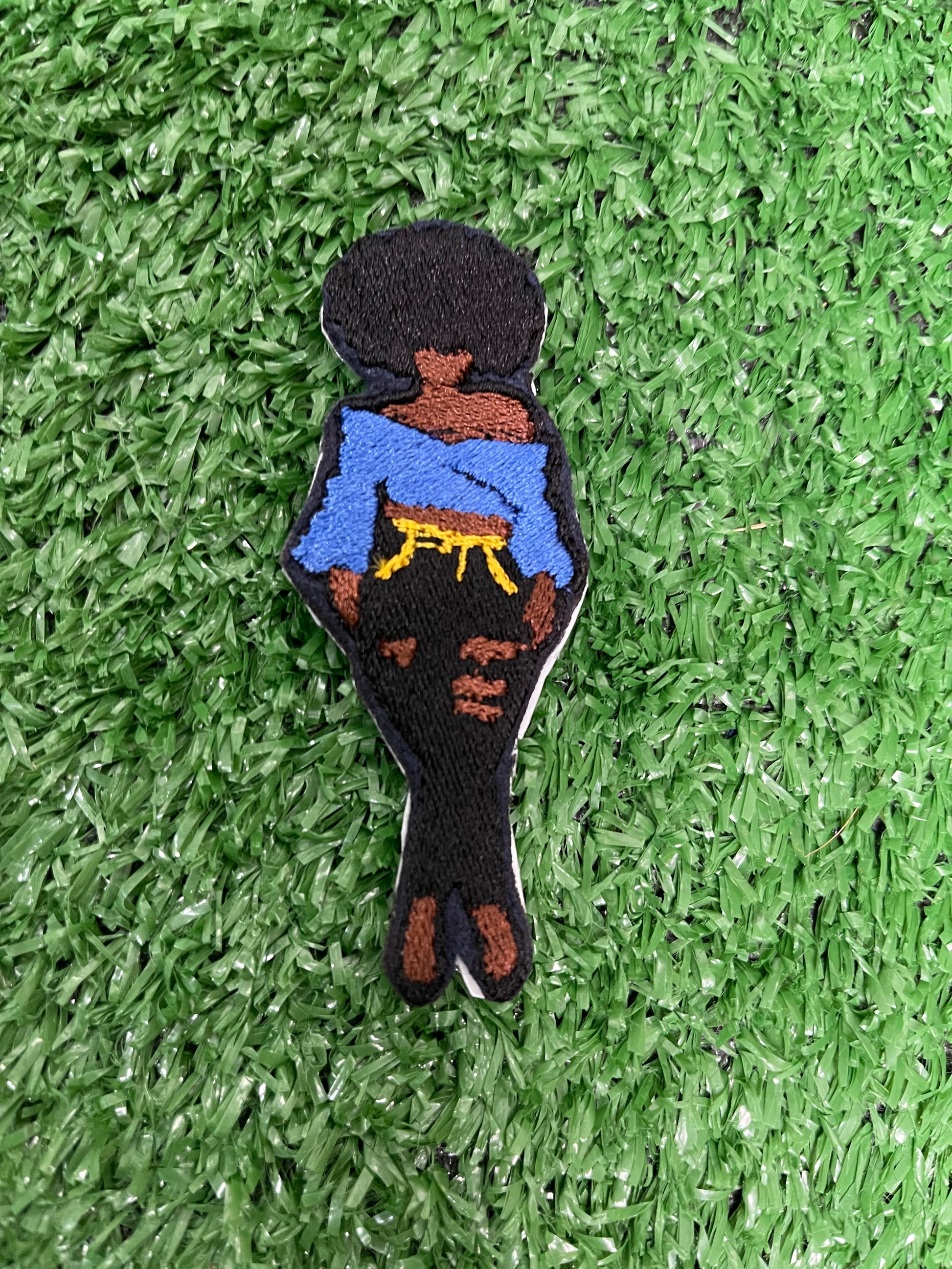 Embroidered iron-on patch of a confident Black woman with a voluminous afro, wearing an off-the-shoulder royal blue top, ripped black high-waisted jeans with yellow stitching details, and black pointed heels. She is standing with one leg slightly crossed in a stylish, relaxed pose.
