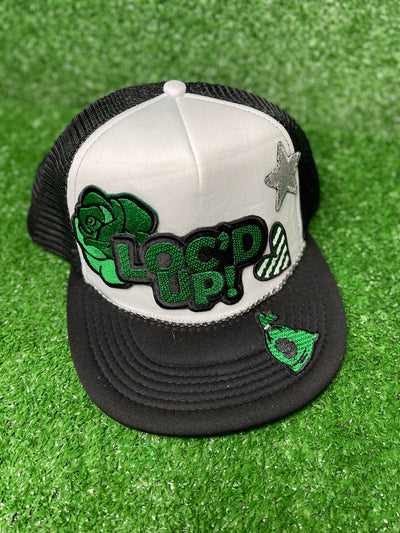 White & Black trucker hat with the text 'Loc’d Up' embroidered in bold black and green letters with other accent patches. The hat features a classic mesh back and adjustable snap closure, perfect for showcasing your locs with style.White & Black trucker hat with the text 'Loc’d Up' embroidered in bold black and green letters with other accent patches. The hat features a classic mesh back and adjustable snap closure, perfect for showcasing your locs with style.