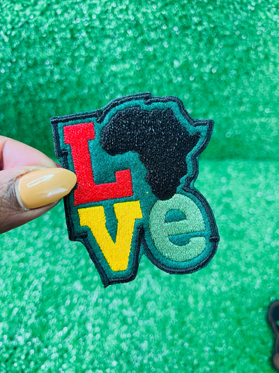 Colorful embroidered iron on patch spelling LOVE with the African continent as the "O" in red, yellow, green and black tones, bold and vibrant design.