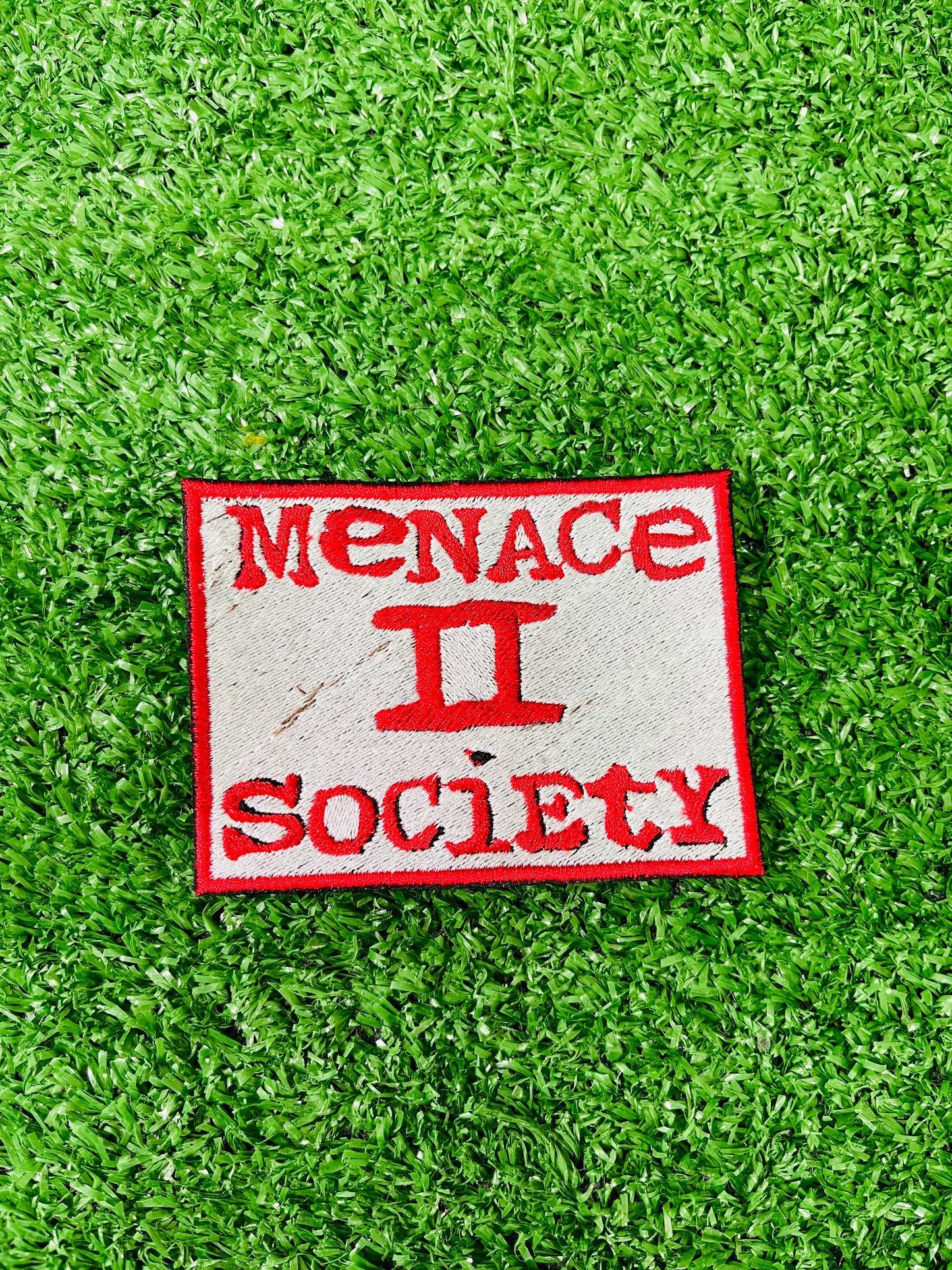 Patch with 'Menace II Society' text on green grass. Squared embroidered iron-on patch with red border and red text reading Menace II Society on a white background.