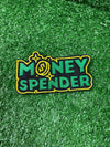 Embroidered iron-on patch reading Money Spender in bold stylish lettering. The patch showcases clean stitching and vibrant green and yellow colors, perfect for customizing clothing or trucker hats.