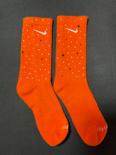 Orange Nike socks embellished with sparkling rhinestones, adding a touch of bling and style.  The socks feature a bold orange color with rhinestones carefully placed for a dazzling effect, perfect for elevating any sneaker look.