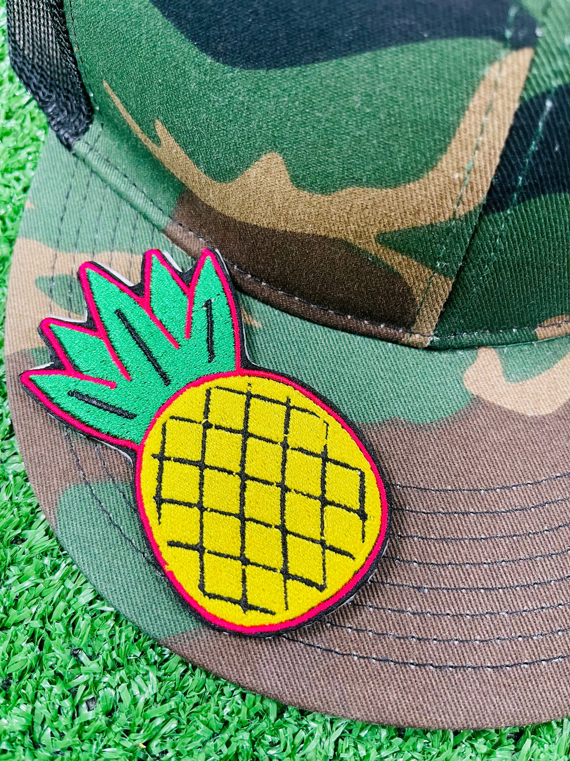 Camouflage cap with a pineapple patch on grass