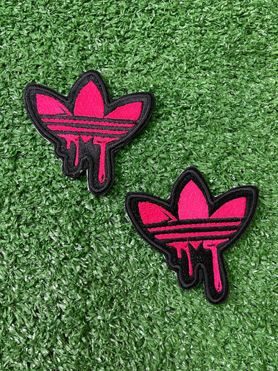 Detailed view of a pink Adidas iron-on patch with the classic trefoil logo and three stripes, perfect for adding a stylish, personalized touch to clothing.