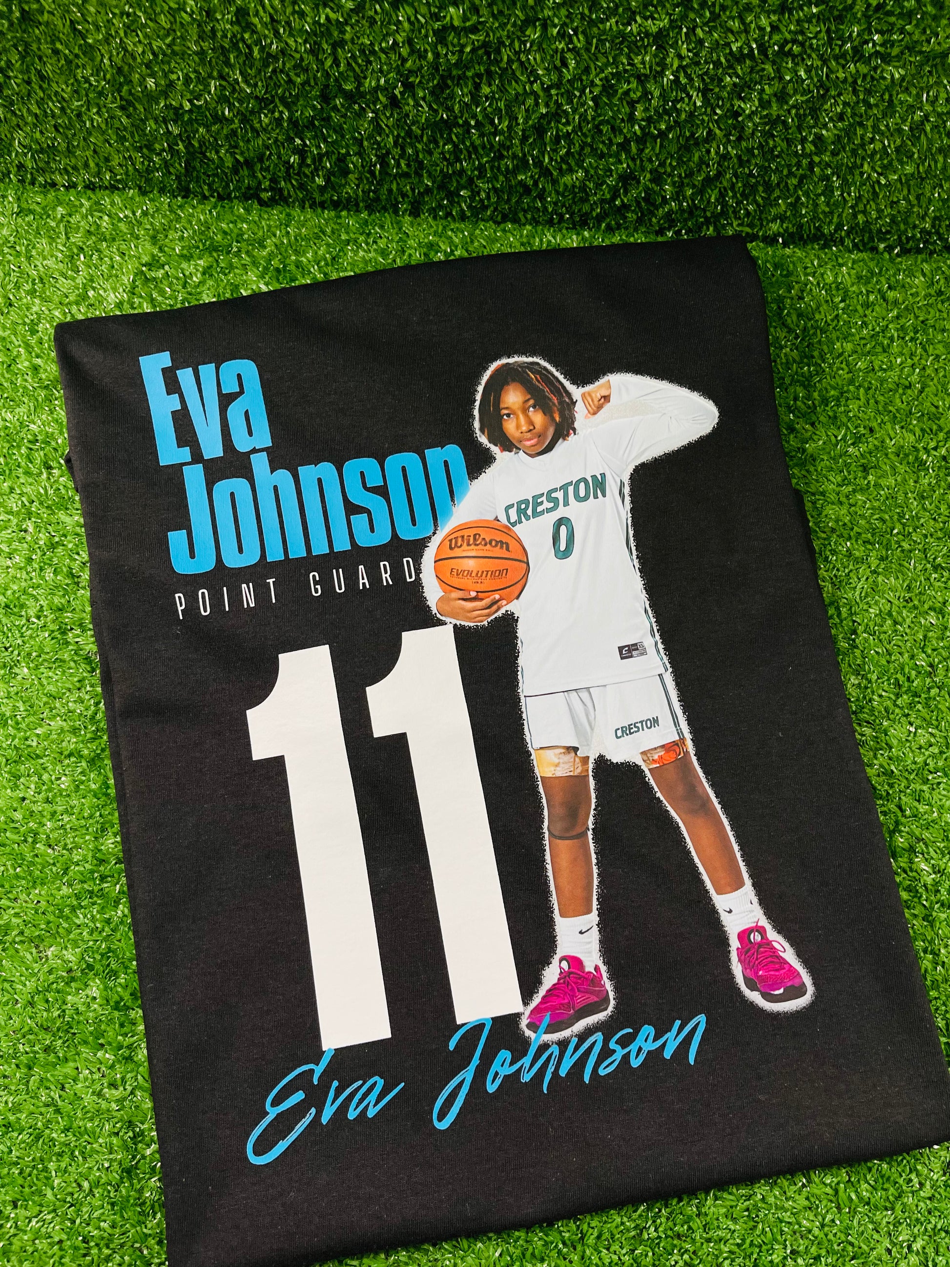 Custom black basketball shirt featuring a young female atahlete in uniform holding a basketball with her name Eva Johnson position, and jersey humber printed in bold graphic text. 