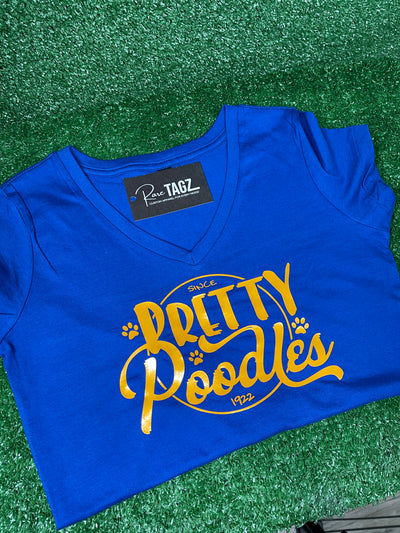 A vibrant blue shirt featuring a stylish 'Pretty Poodle' graphic. The text is elegantly displayed in shimmering gold/yellow font, creating a stunning contrast against the blue background. Sigma Gamma Rho Sorority