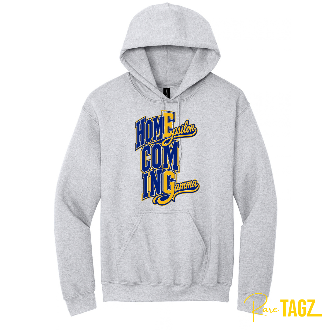 A light heather gray pullover hoodie with a 'Homecoming Gamma' graphic printed on the chest in blue and yellow, shown against a plain white background.