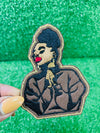 An embroidered patch featuring a black woman with a high puff hairstyle, bold red lips and a serene expression.