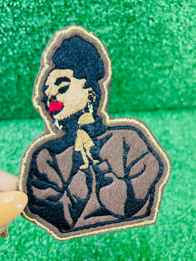 An embroidered patch featuring a black woman with a high puff hairstyle, bold red lips and a serene expression.