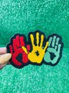 A vibrant embroidered patch featuring three overlapping handprints in red, yellow, green, symbolizing unity. pride, and heritage. The patch has a bold black outline that enhances the striking design. Perfect for celebrating Black culture and adding a meaningful touch to clothing or accessories.