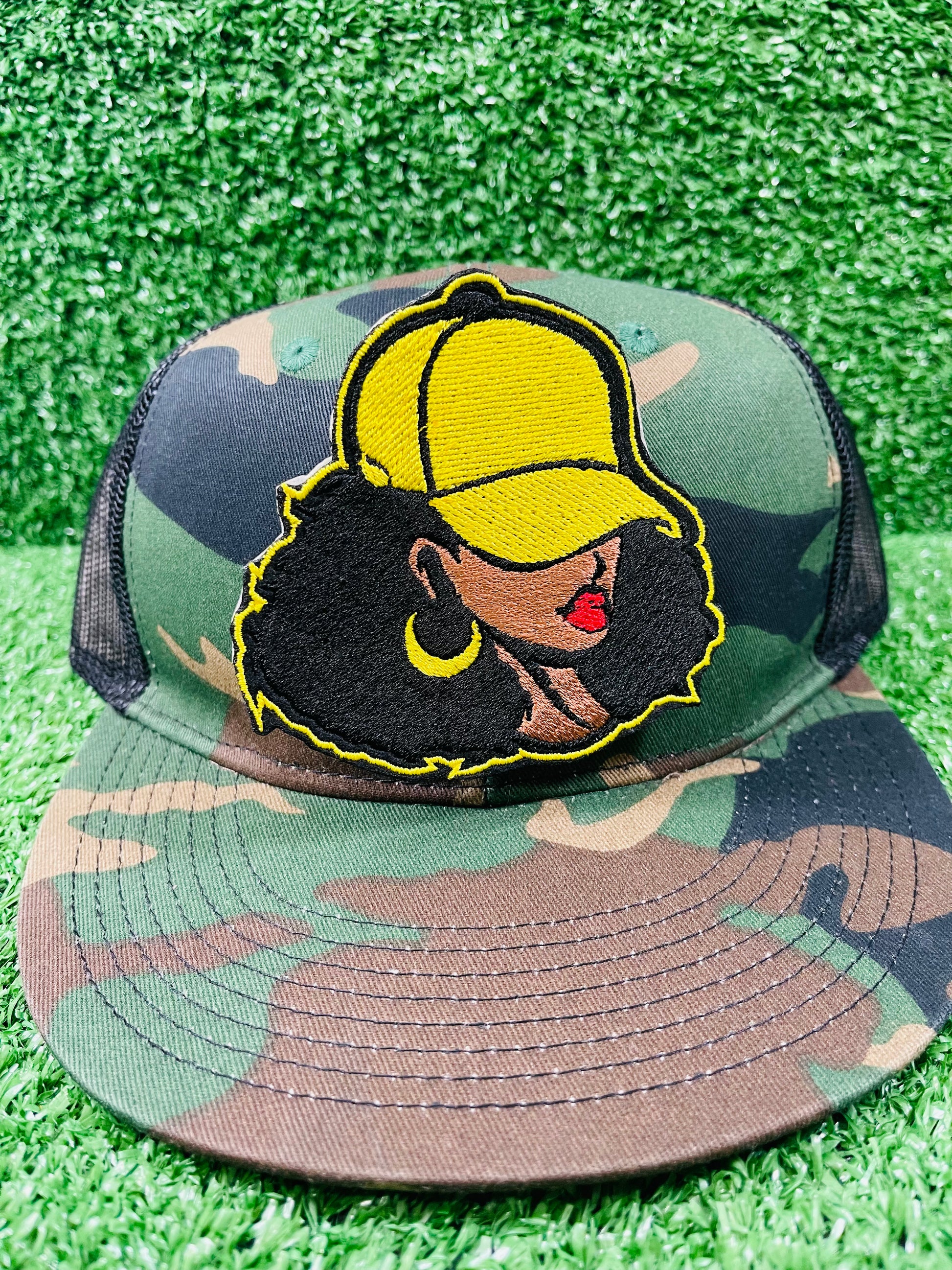 Camouflage bucket hat with a decorative patch on a grassy background