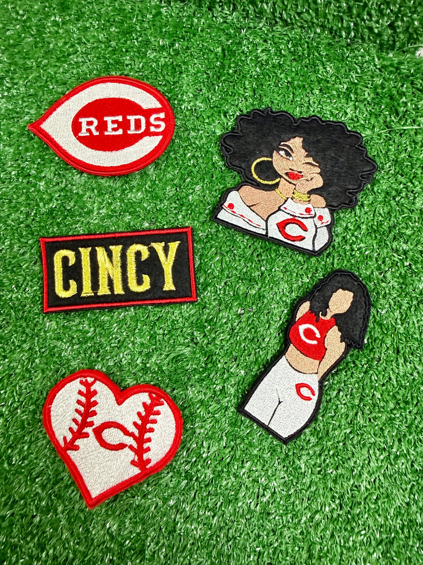 Collection of patches with 'Reds', 'Cincy', and heart designs on a green background